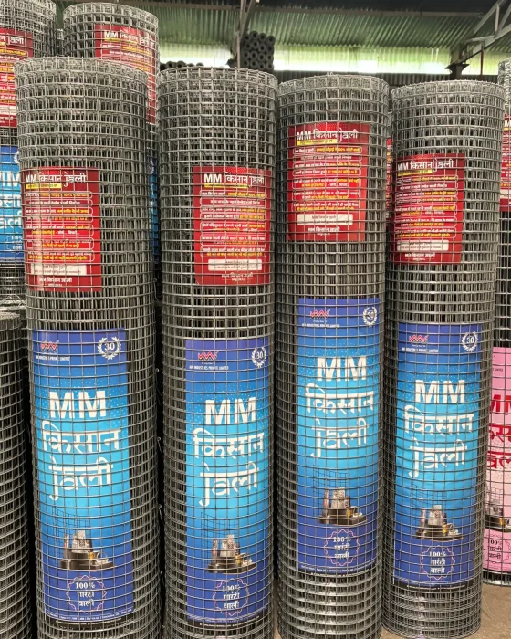 Several large rolls of steel wire mesh with blue and red labels are standing upright on a warehouse floor.